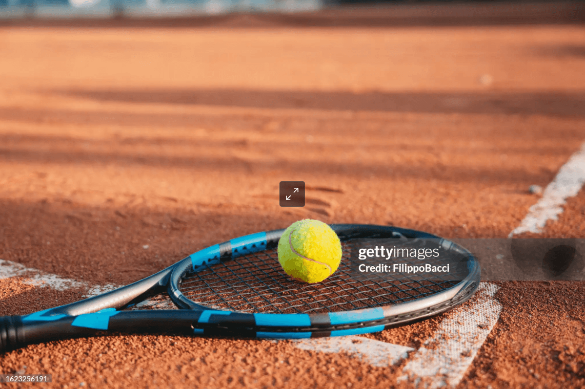 Raqueta y pelota de tenis sobre polvo de ladrillo
